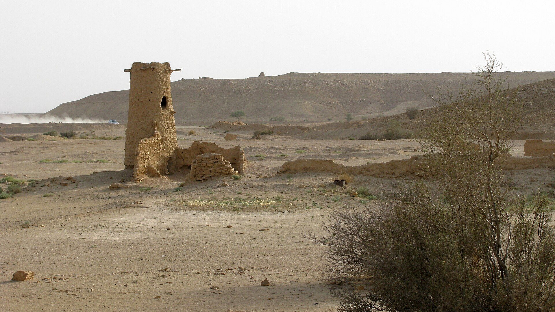 A lone stone watchtower on the desert near Al Barrah, with the Tuwaiq escarpment on the horizon